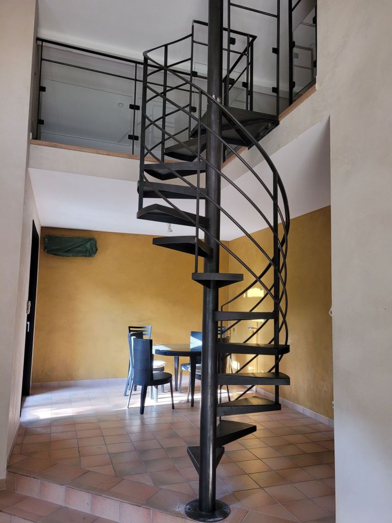 Escalier hélicoïdal en métal finition brut ciré avec garde-corps débillardé, et garde-corps de trémie avec soubassements vitrés . Réalisation sur Brignais dans la région Lyonnaise. escalier soudé sur un chantier