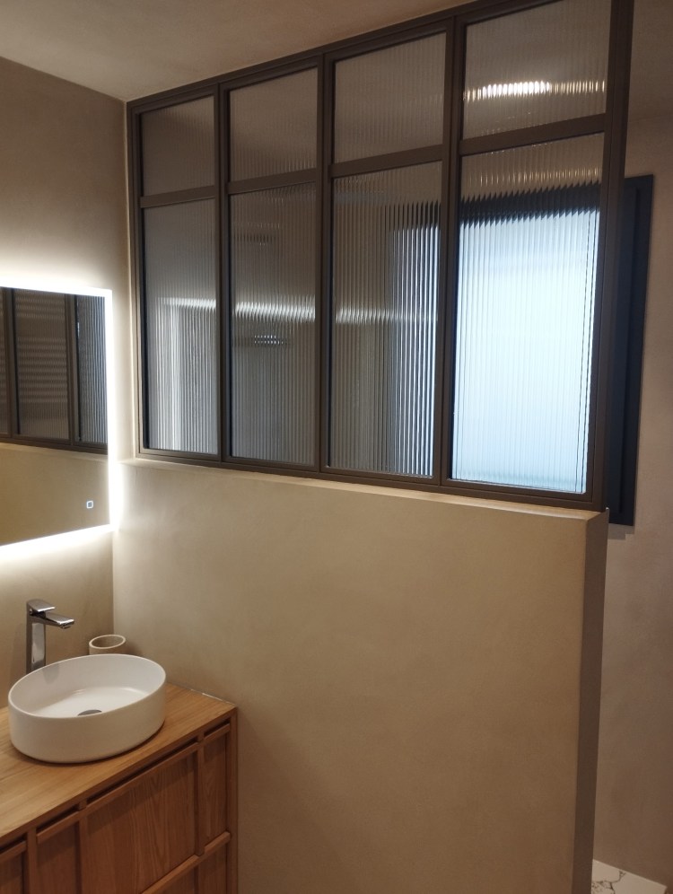 verrière avec verre strié type vitrage flute dans salle de bain en béton ciré